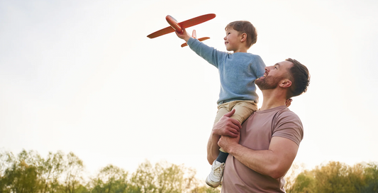 Padre sosteniendo a su hijo en los hombros mientras juega con un avión de juguete, simbolizando momentos especiales del Día del Padre