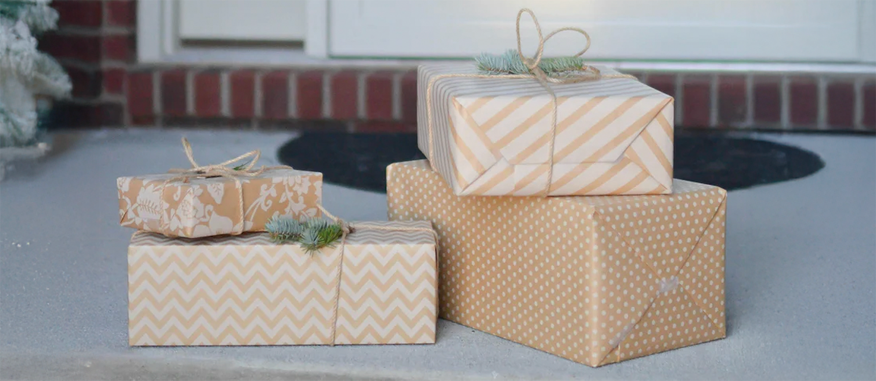 Cuatro cajas de regalo envueltas con papel beige y blanco con diferentes patrones navideños, colocadas sobre el suelo frente a una puerta ideas visuales para regalos de Navidad.